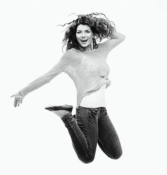 Foto en blanco y negro de una chica con el pelo rizado y ropa casual saltando.