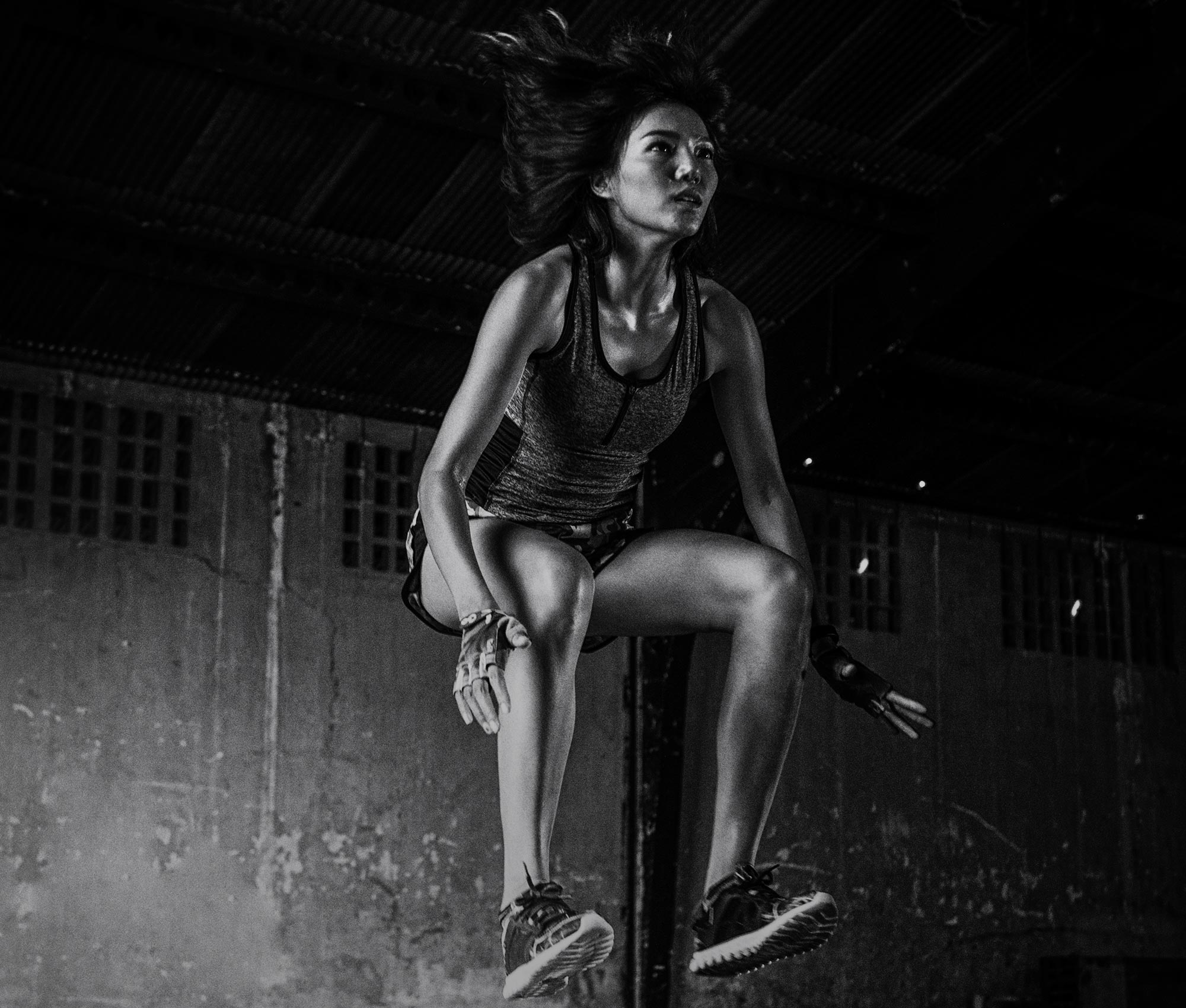 Imagen en blanco y negro de una chica asiática con ropa deportiva saltando.